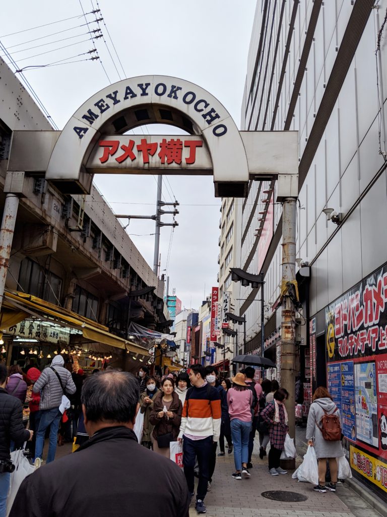 busting Japanese shopping street, Ameyokocho. There is a stone arch above the street with the name written on it.