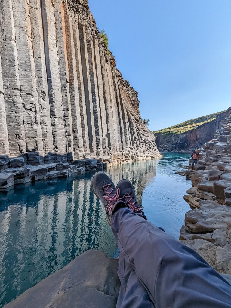 Looking out over Gabi, The Fringe Explorers legs and a turquoise river at a basalt canyon wall