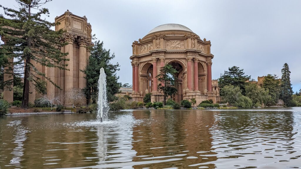 Looking across a lake at the Palace of Fine Arts, the Palace features brown and rust color roman style dome and columns