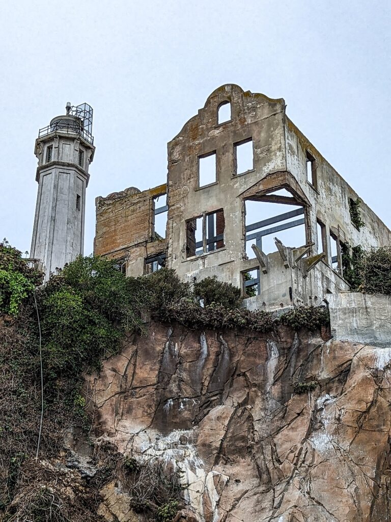 Looking up at a ruined concrete building on Alcatraz island next to a concrete lighthouse