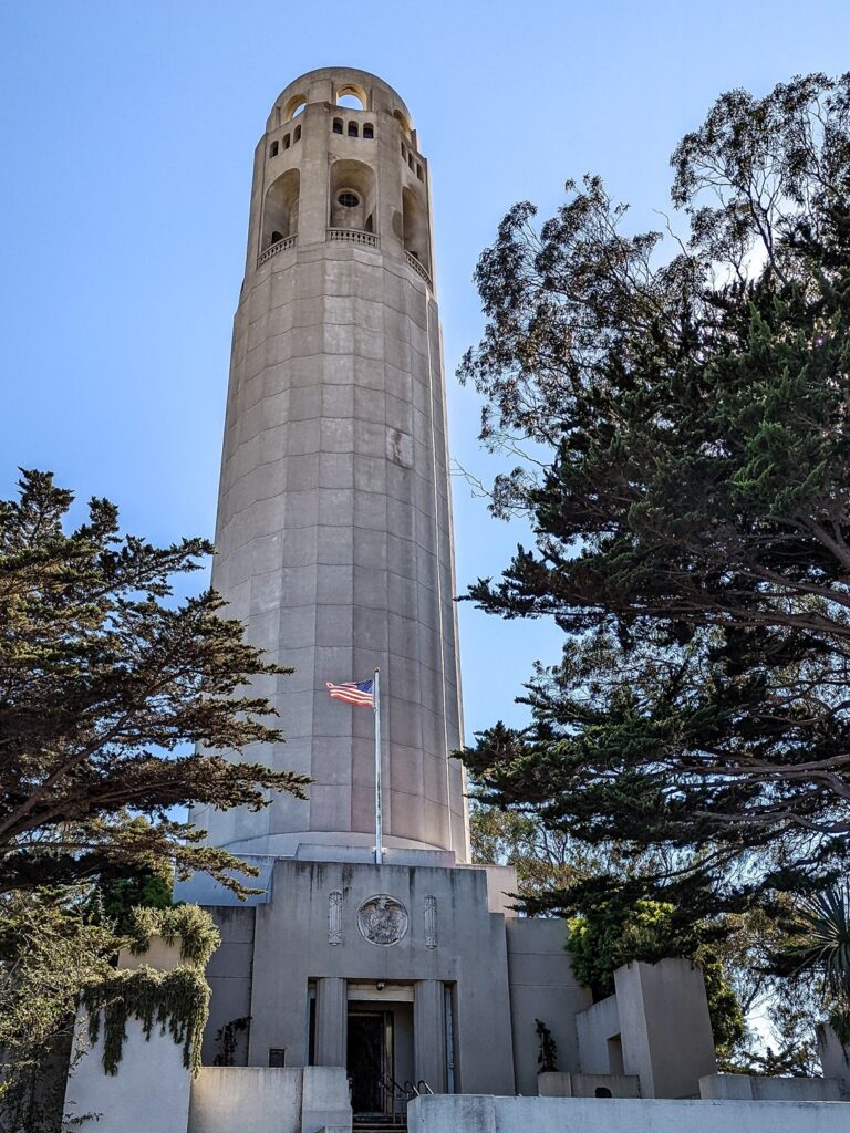 Looking up a white stone tower that has an American flag at it's base