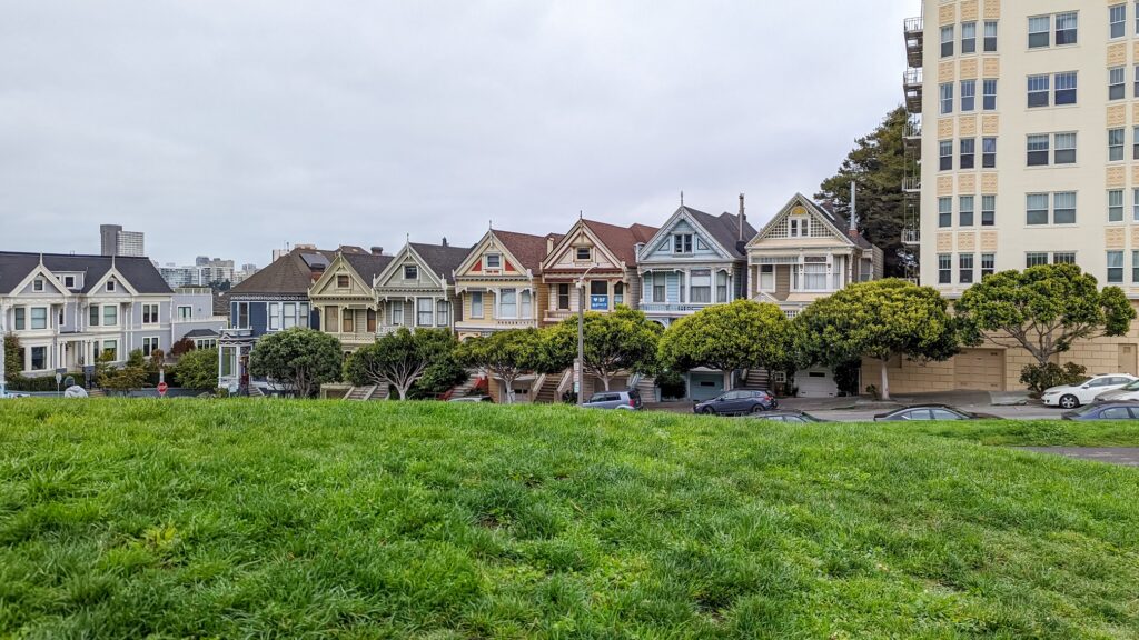 Row of colorful Victorian style homes on the opposite side of a green grass hill