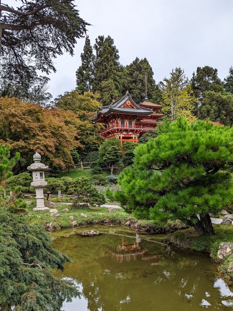 Japanese style red-orange pagoda in the background surrounded by a pond and trees.