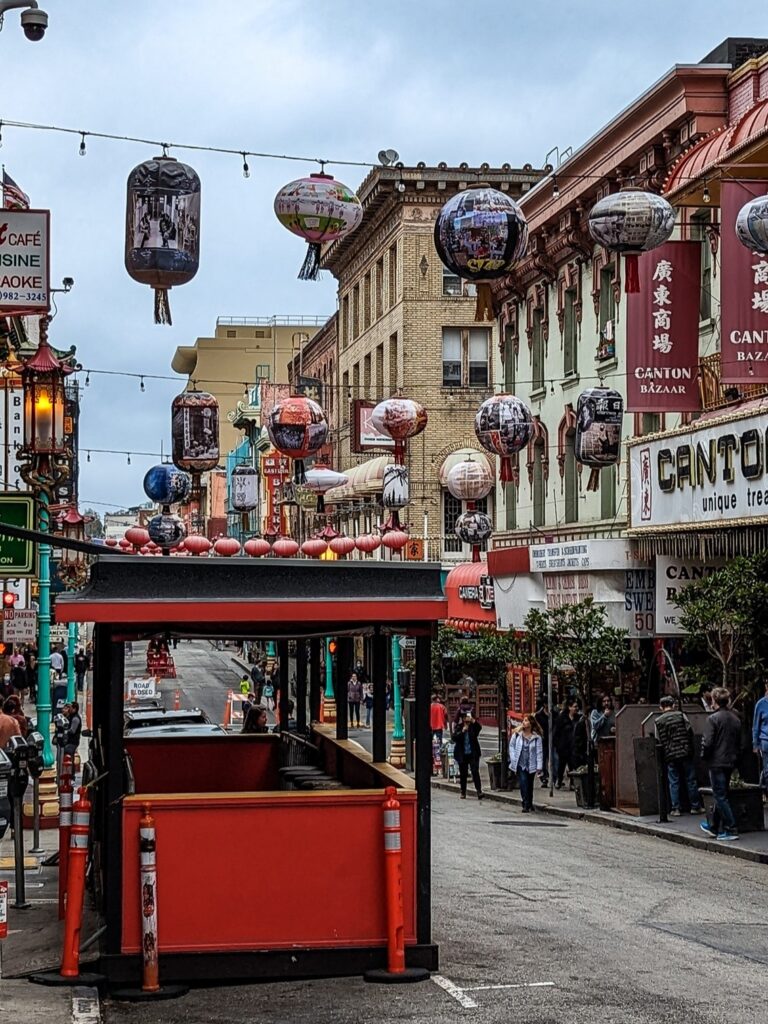 Looking down a street in Chinatown that has brown and red brick buildings and colorful landers strung over the street