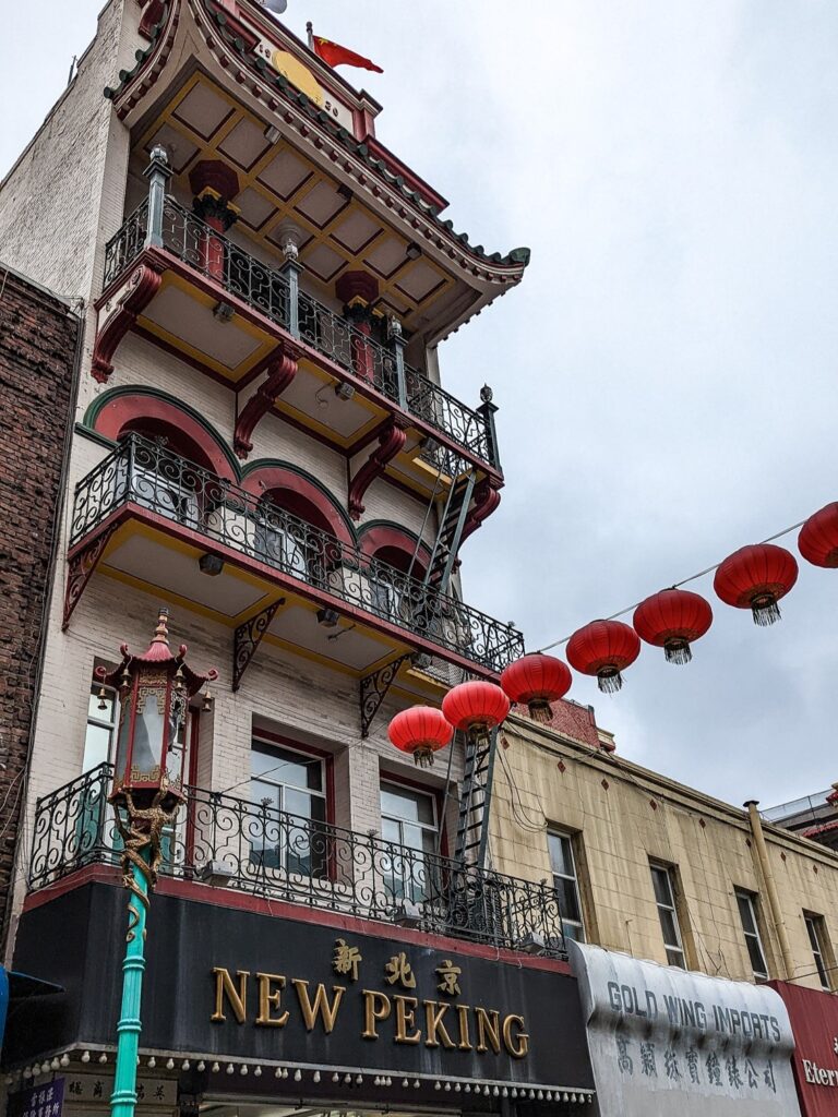 Looking up at an Asian style building with red lantern strung across the street to the building.