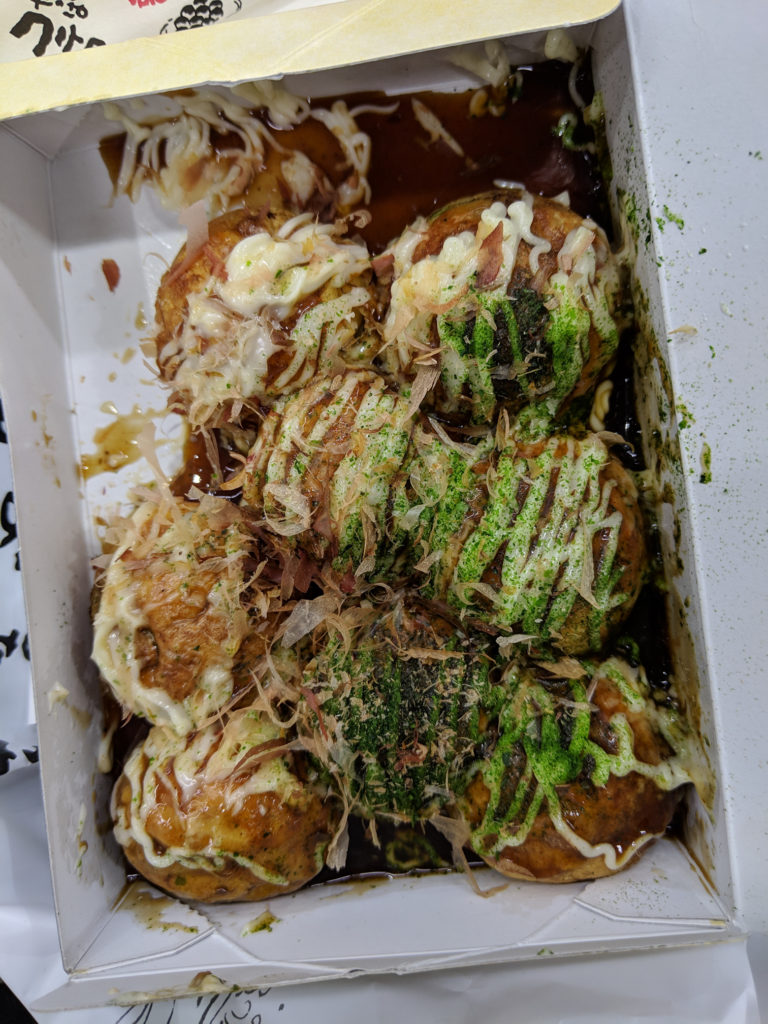 takoyaki - 8 takoyaki fried balls in a paper container with Japanese mayo drizzled on top with bonito flakes and green seaweed flakes