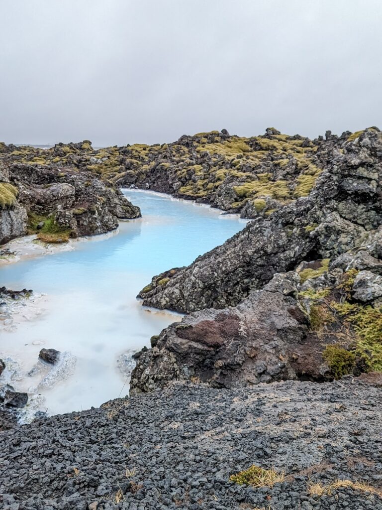 milky blue hot spring pool surrounded by volcanic rocks and moss