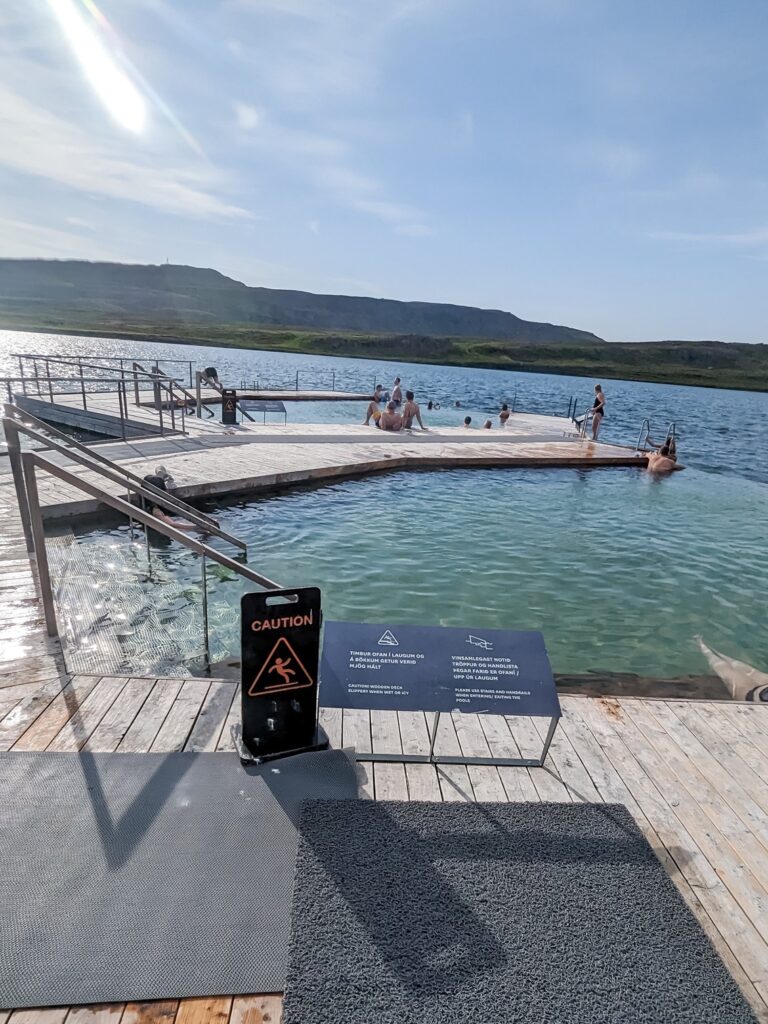 two separate hot spring pools on the edge of a lake partially surrounded by wood walkway