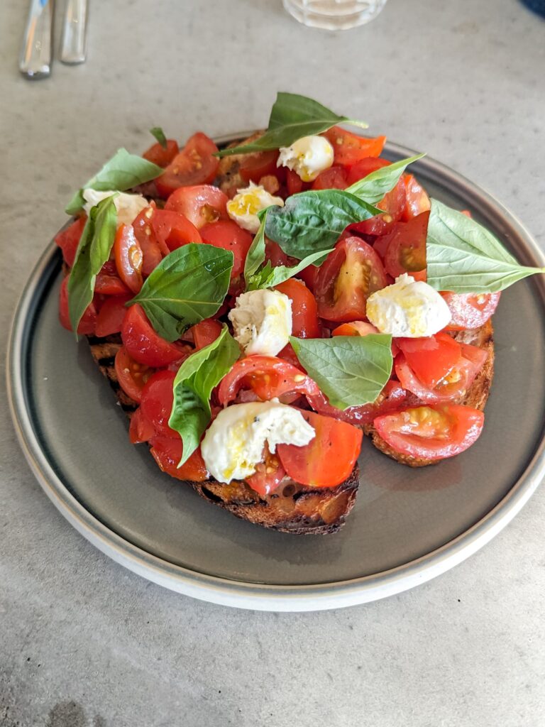 Bruschetta - red tomatoes, mozzarella balls and basic on top of some crunchy toast sitting on a beige plate