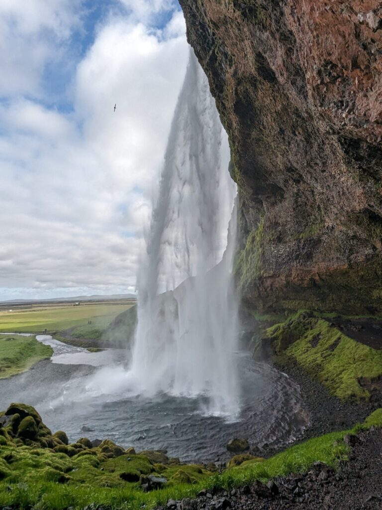 Side view of a large waterfall spilling over a brown and mossy mountainside.