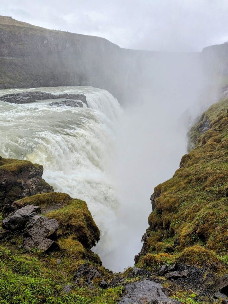 Large waterfall cascading over a cliff covered in moss. The waterfall is creating a cloud of mist.