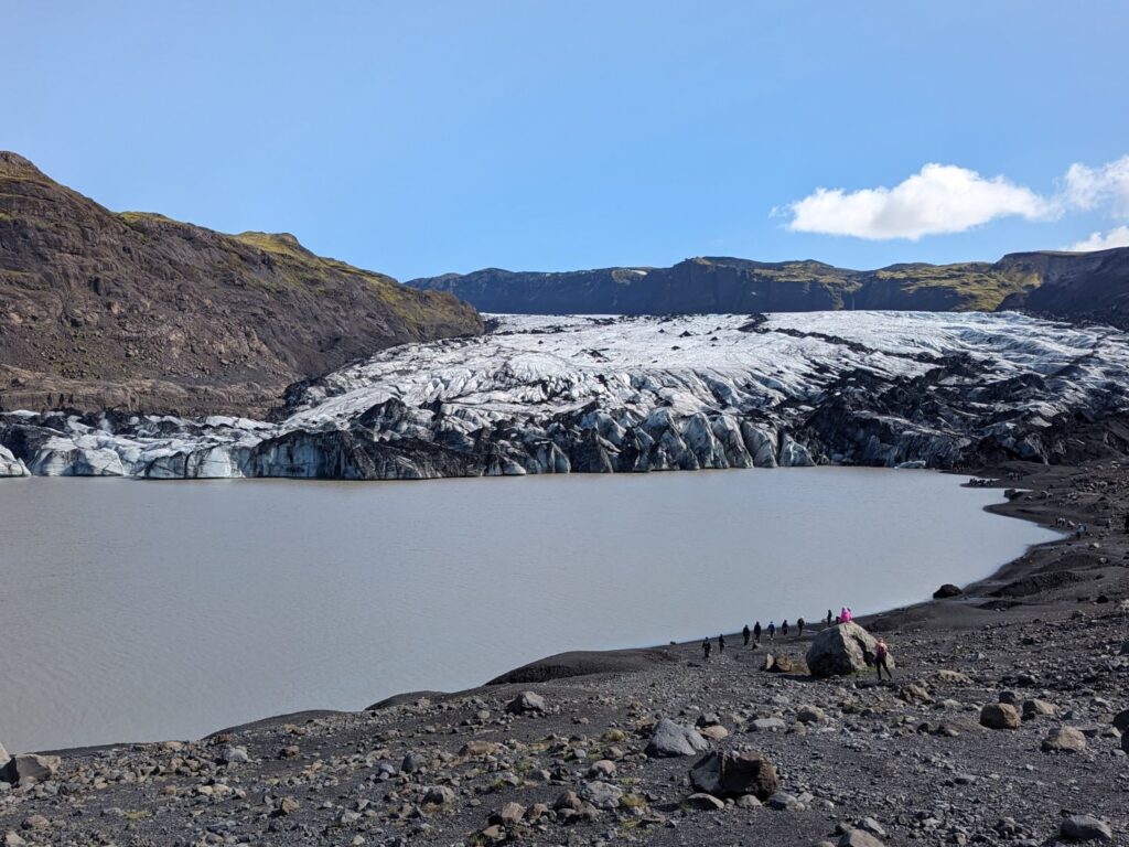 a glacier between rocky mountains extending out into a glacial lake