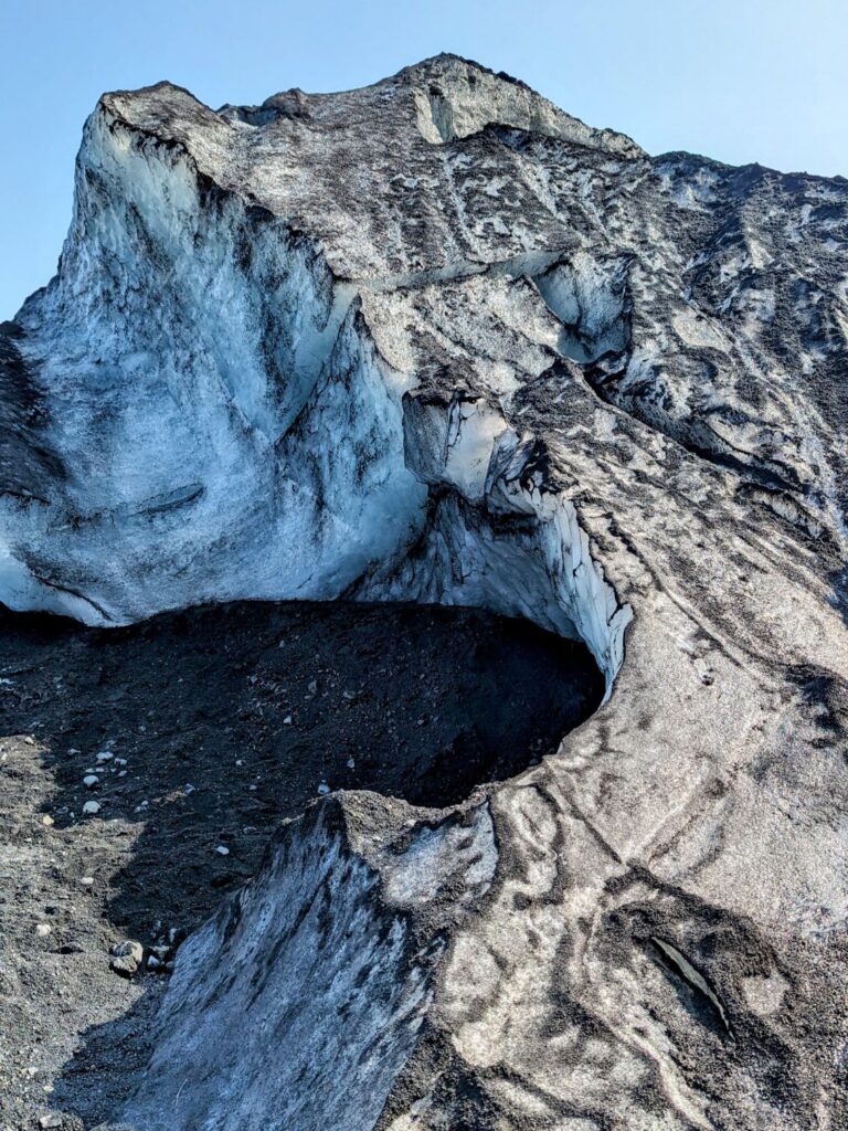 up close photo of a glacier with black sand scattered across it