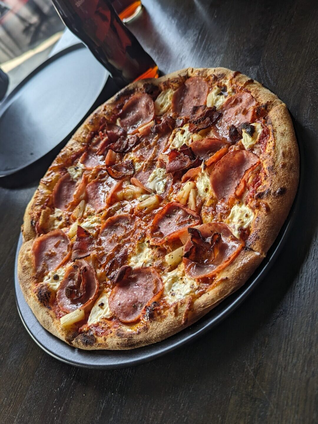 Ham and pineapple pizza cut into six slices. Sitting on a metal tray. Glass soda bottle sit in the background