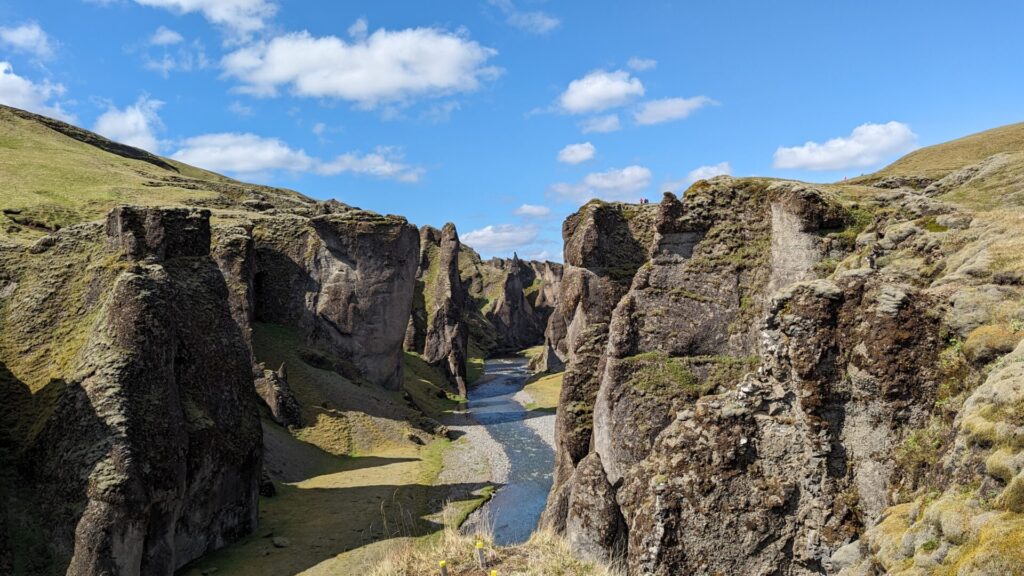 Mossy canyon with a river running down the center. The sky is bright blue with puffy clouds