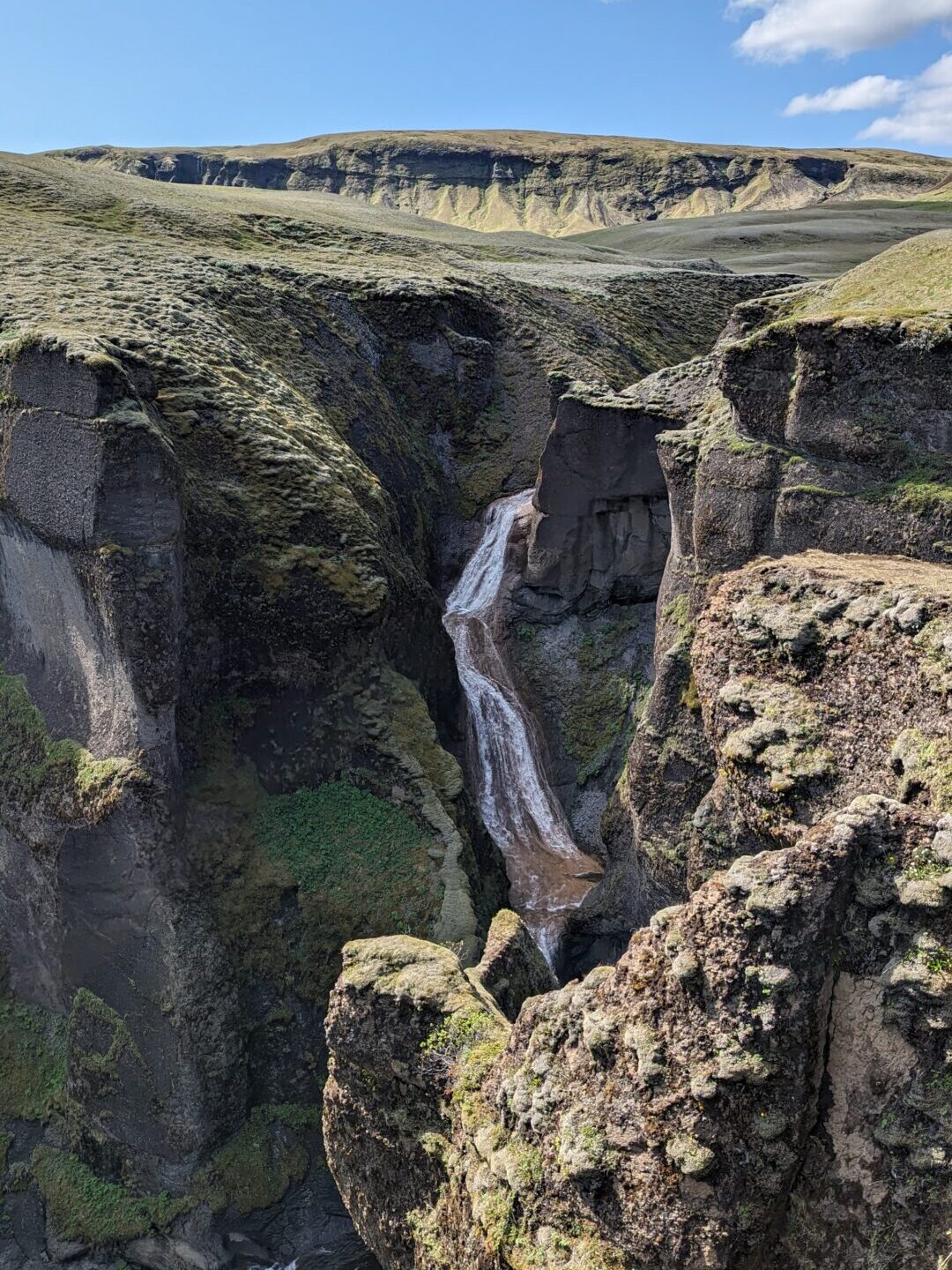 Waterfall cascading over a mossy cliff in a canyon.