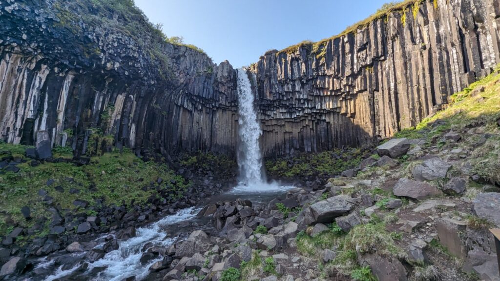 Waterfall cascading over a basalt column cliff into a river.