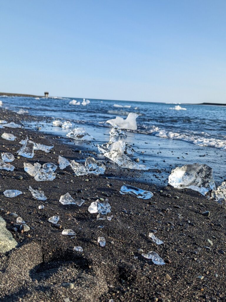 small chunks of ice sitting on the shore of a black sand beach,