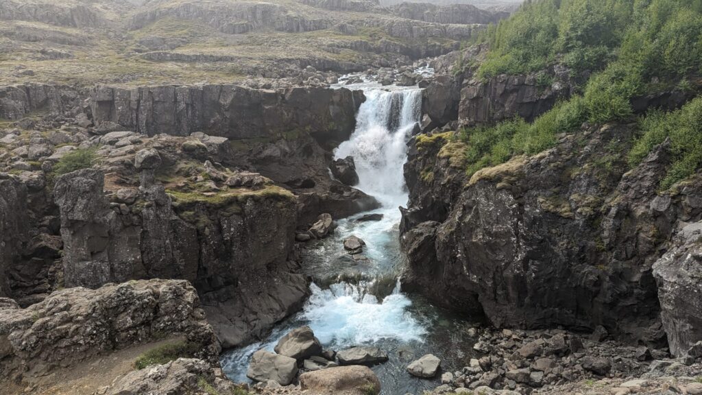 Waterfall rushing over some rocky cliffs into a river.