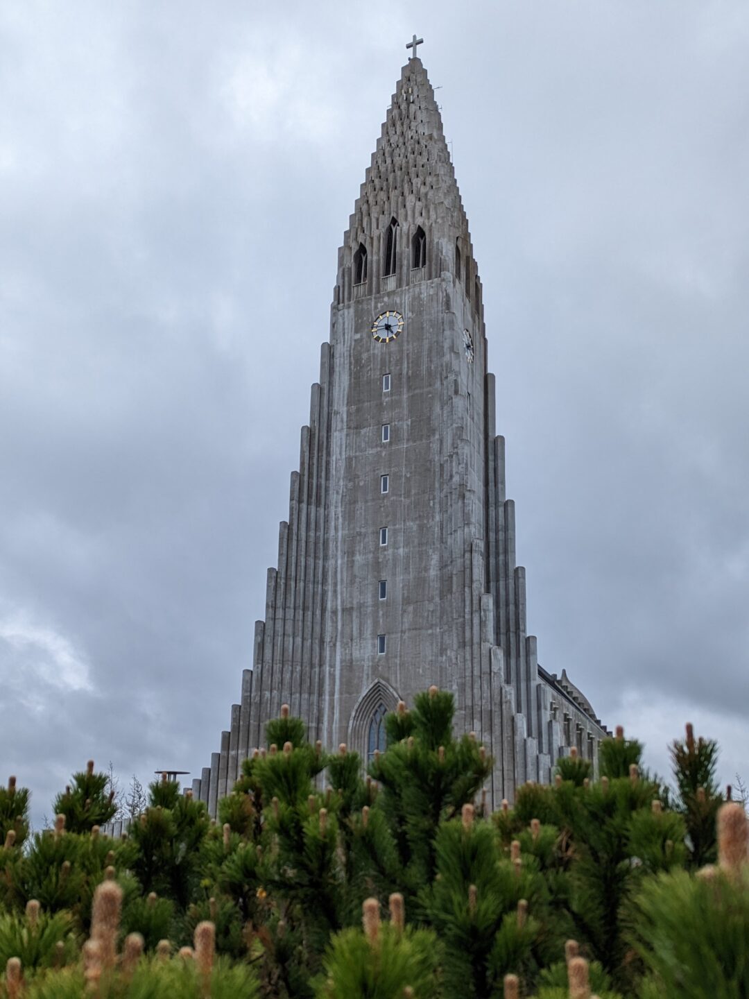 Church made made of grey stone with a staircase like architecture.  Near the top there is a clock and then windows above the clock. There is a cross on the very top.