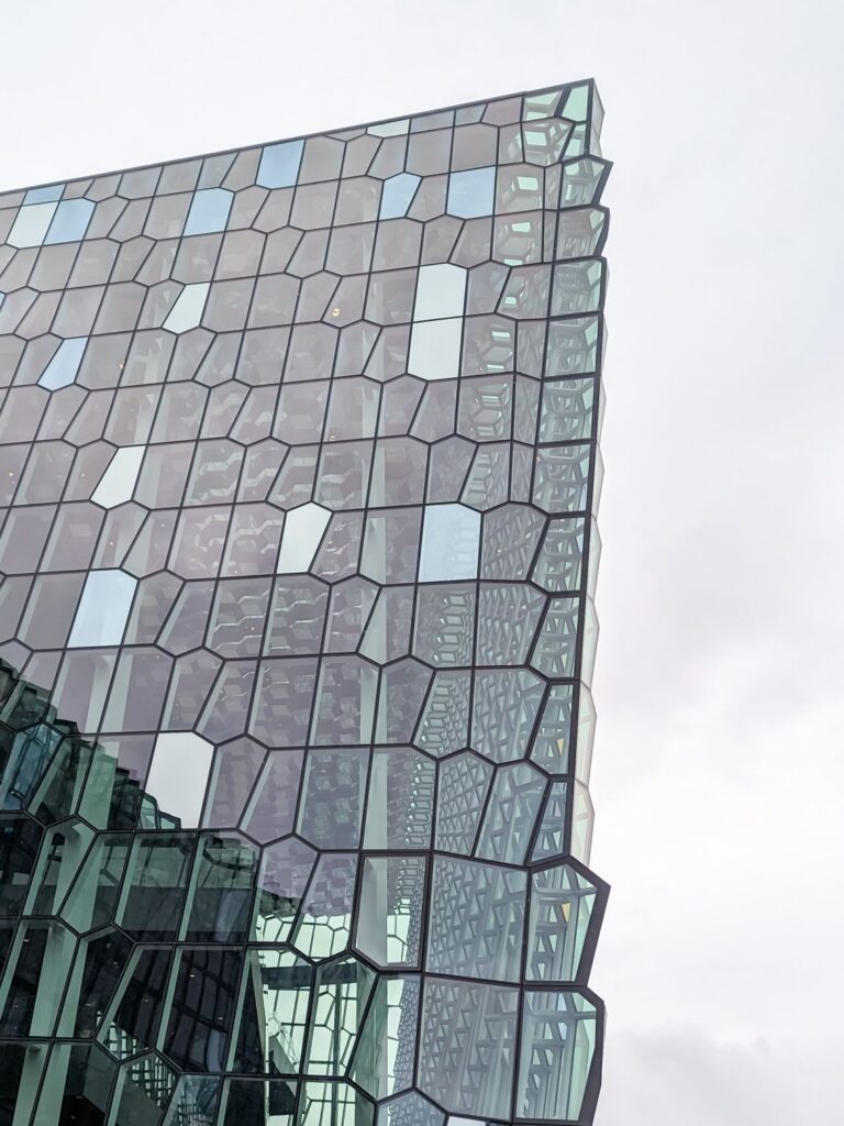 Top corner of a glass building that looks like a honeycomb of glass put together to make walls.