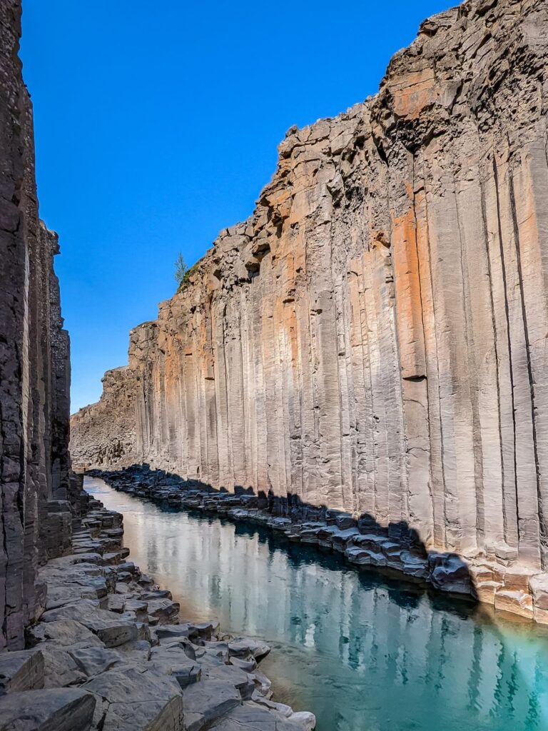 Grey and orange basalt column canyon with a turquoise glacial river running through the center