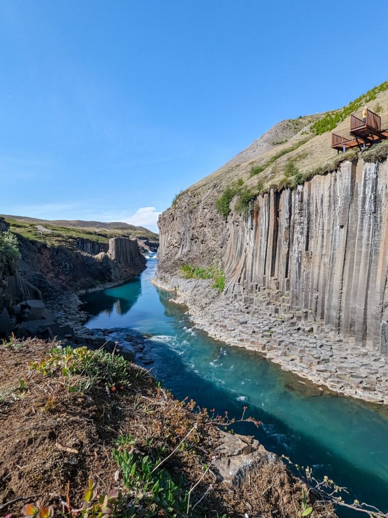 Grey and orange basalt column canyon with a turquoise glacial river running through the center