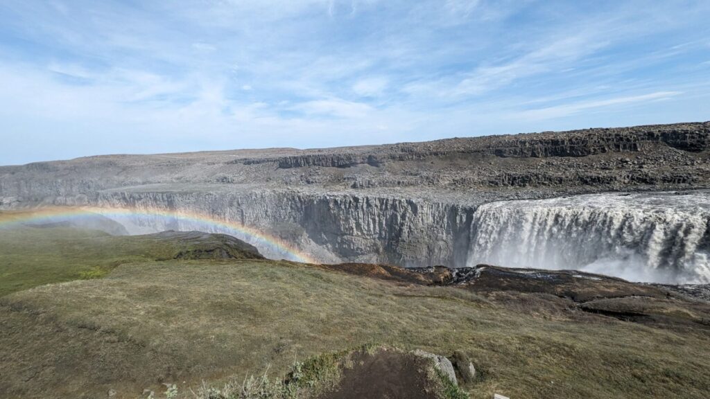 Large waterfall cascading over a cliff to the right and a rainbow in the waterfall mist to the left