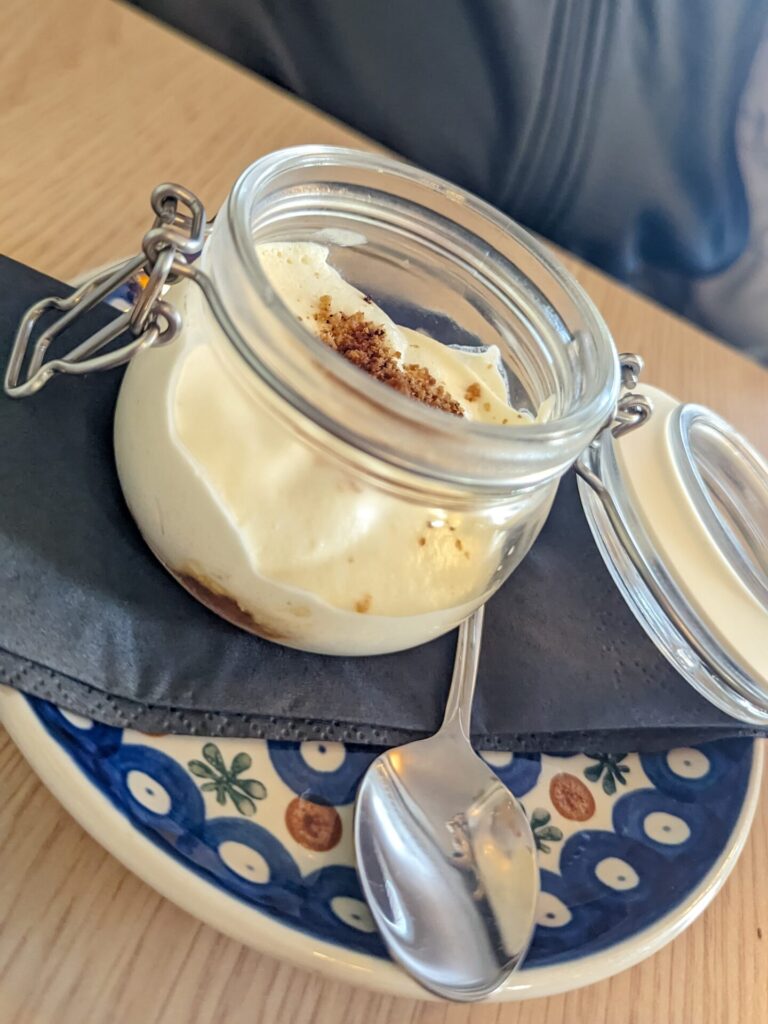 White cream dessert inside a little glass jar sitting on a plate with a napkin and spoon