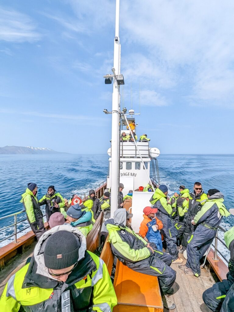 whale watching boat with 20 people all wearing black and lime great jumpsuits.