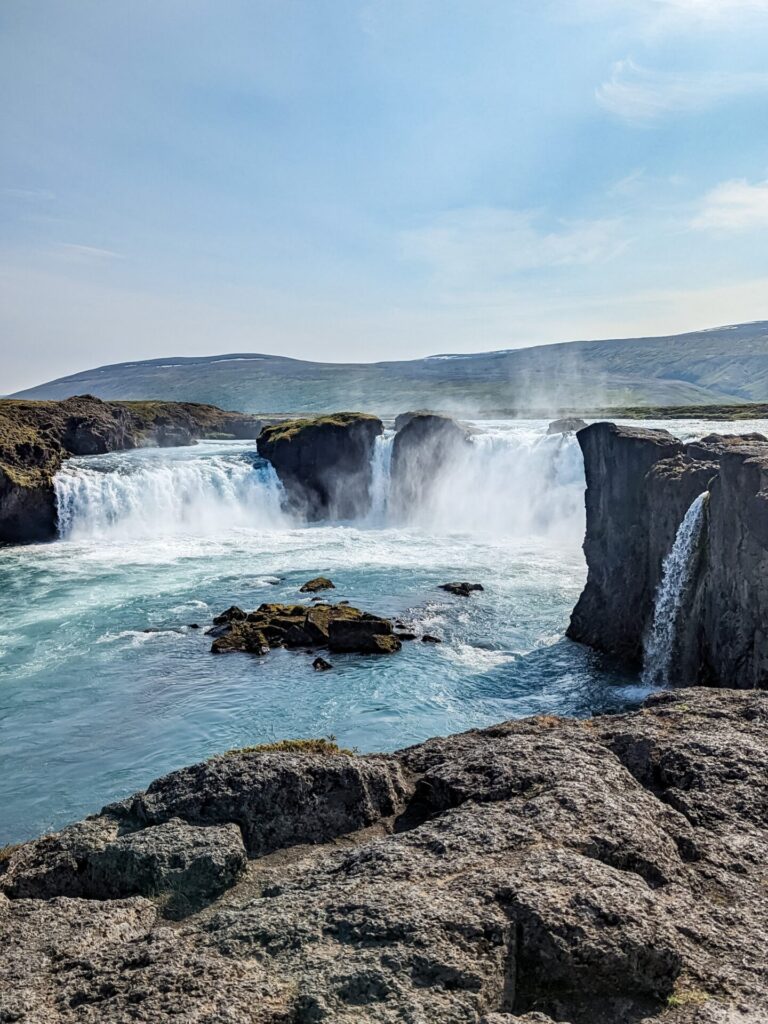 large waterfall cascading over multiple areas of a low cliffside. The water if a bright turquoise blue.