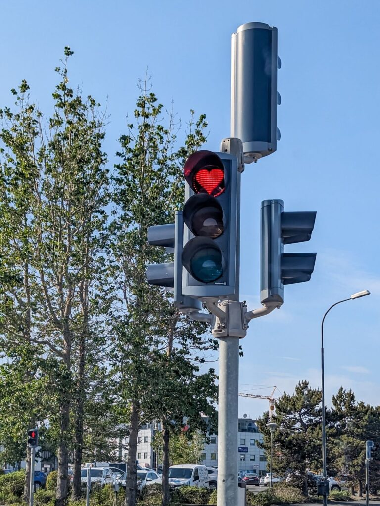 Free standing traffic light with four different indicators facing different directions. The one facing the camera has a red heart for the red light.