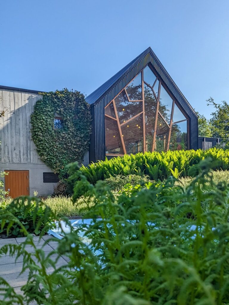 Concrete and black triangle roof building with a large window that has decorative wood through the window mimicking branches.