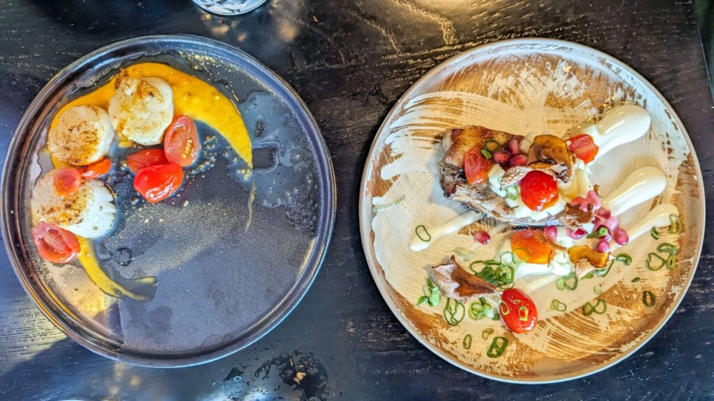 Two plates of food pictures from above. The plate on the left with grey with three scallops, some cherry tomatoes, and an orange sauce. The plate on the right has a white fish with cherry tomatoes and a white sauce,.==.