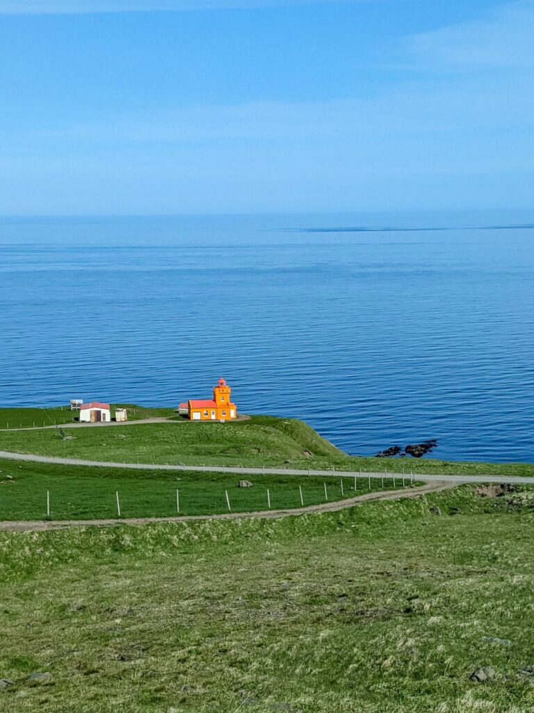 An orange lighthouse on a grassy coastal cliff