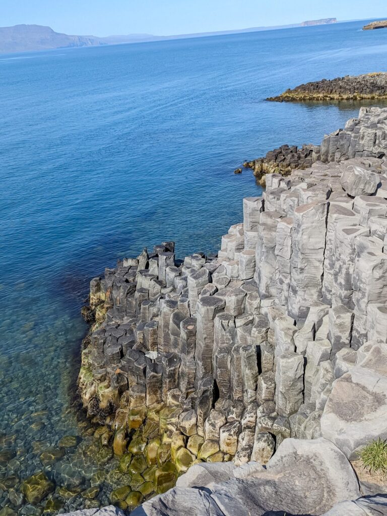 Basalt column cliff along the shore of a fjord. The water hitting the basalt columns is clear and very blue