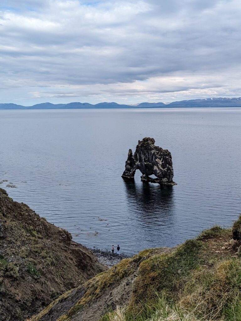 Basalt rock formation just off the shore. It's black, red and has some moss. There are two holes at the bottom of the rock formation