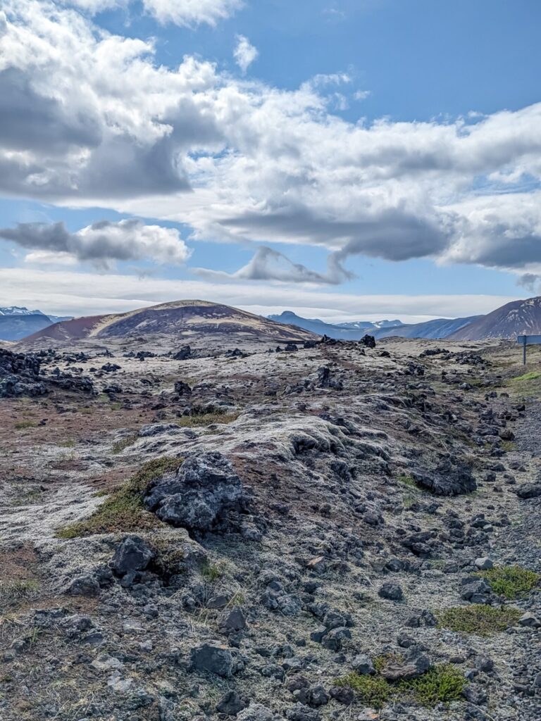 Jagged mossy lava field with a hill and mountains in the background