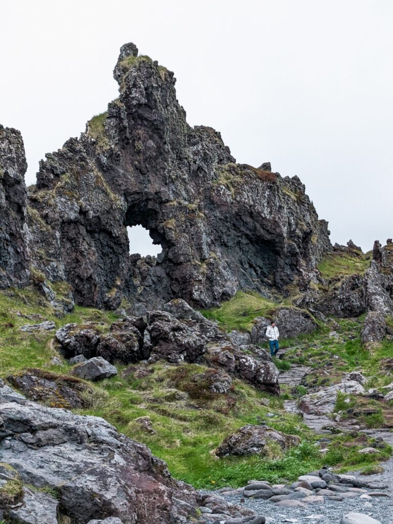 black lava rock formation jutting out of a grassy embankment next to a stone beach.