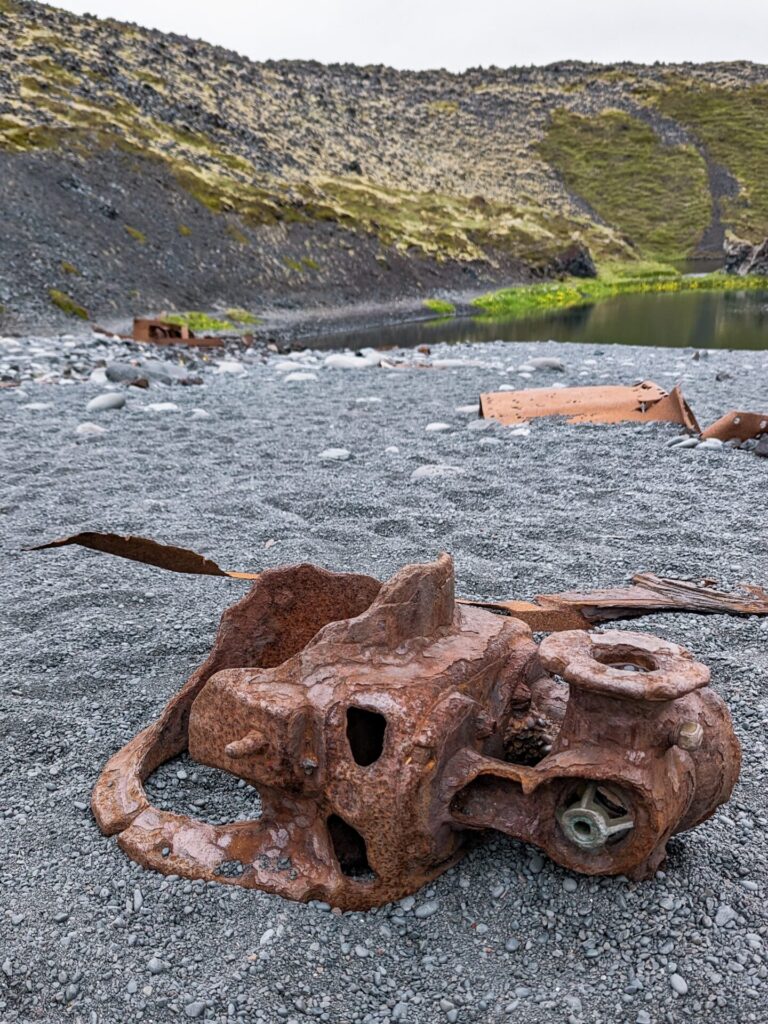 Rusted piece of a boat laying on a black rocky beach.