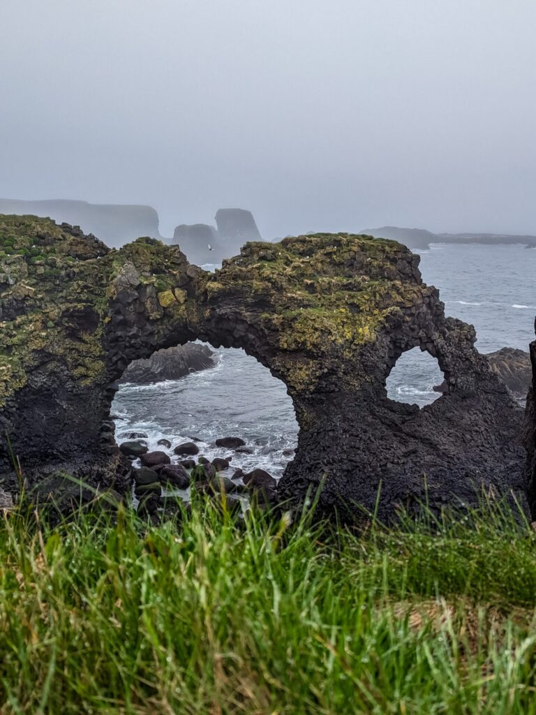 Natural basalt stone arch on the shore with waves crashing underneath it.