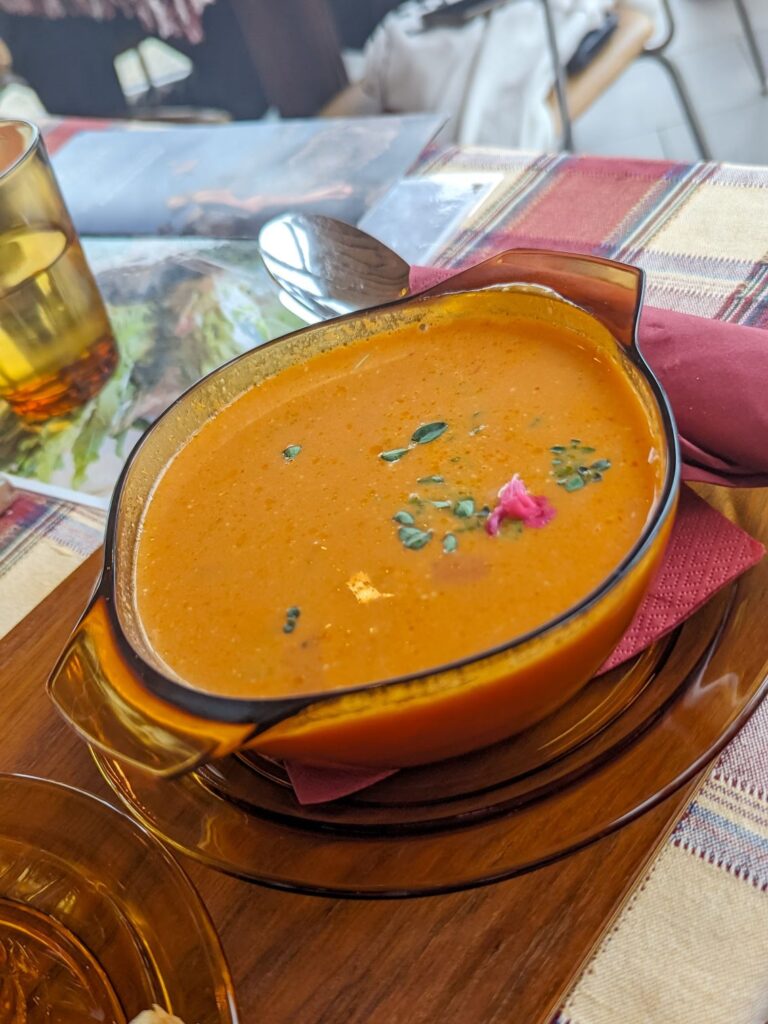 Orange colored fish soup in a brown-ish clear glass bowl with a matching plate underneath.