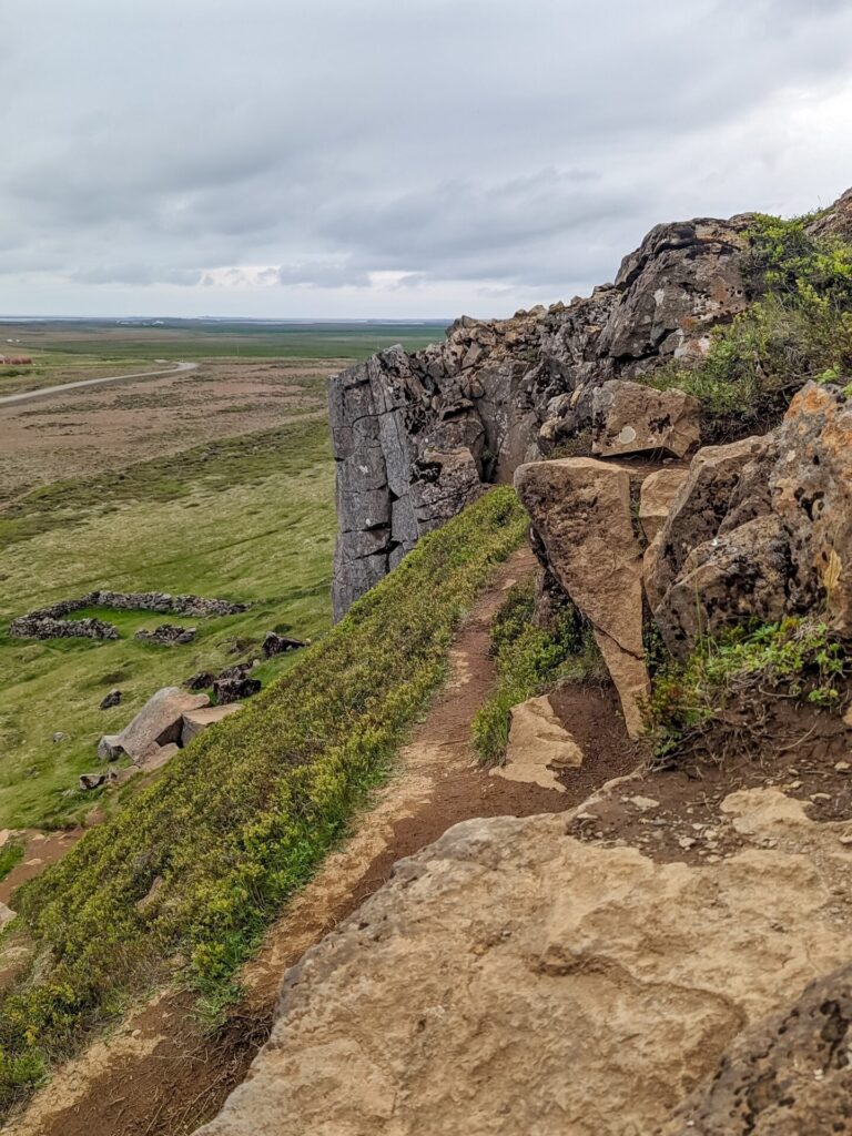 Standing on stop of a basalt cliff looking towards an expansive grass field.