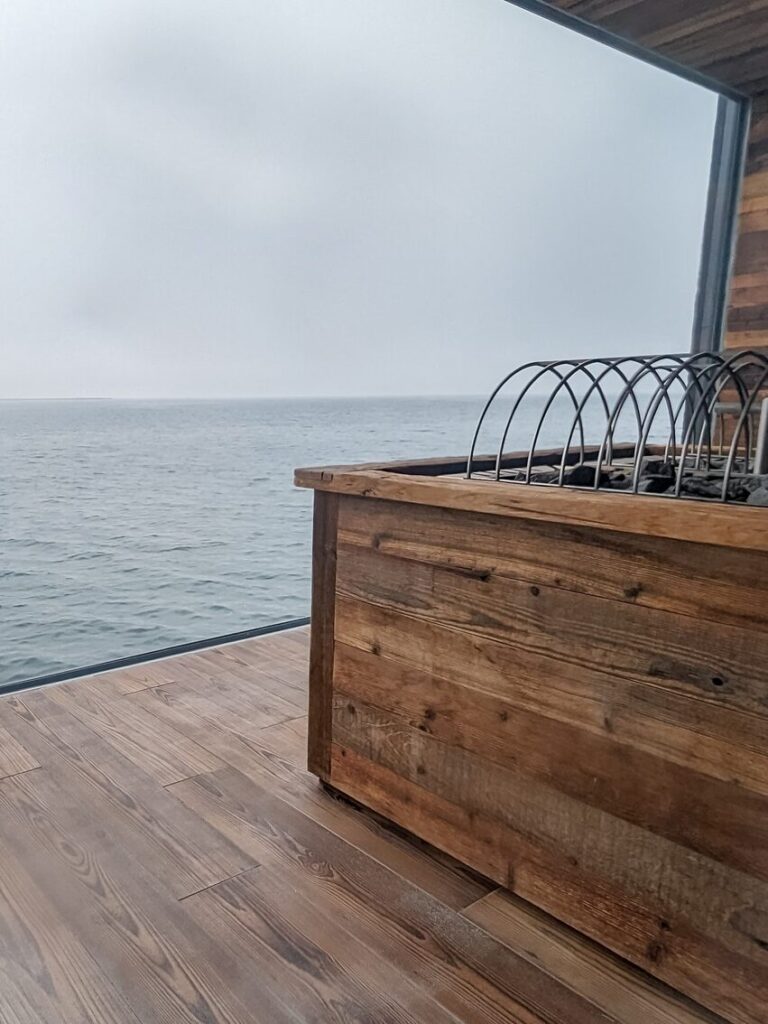 Wood panel sauna with a large glass window looking out into the ocean.