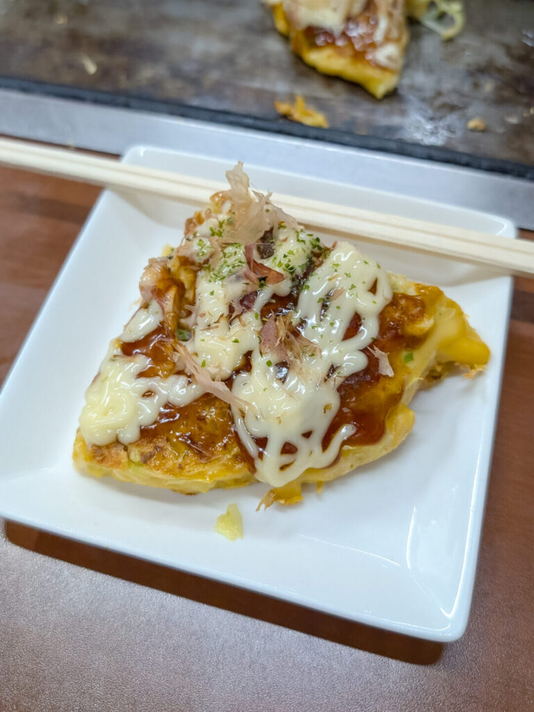 White place with a quarter slice of an okonomiyaki with sauce and Japanese mayo on top