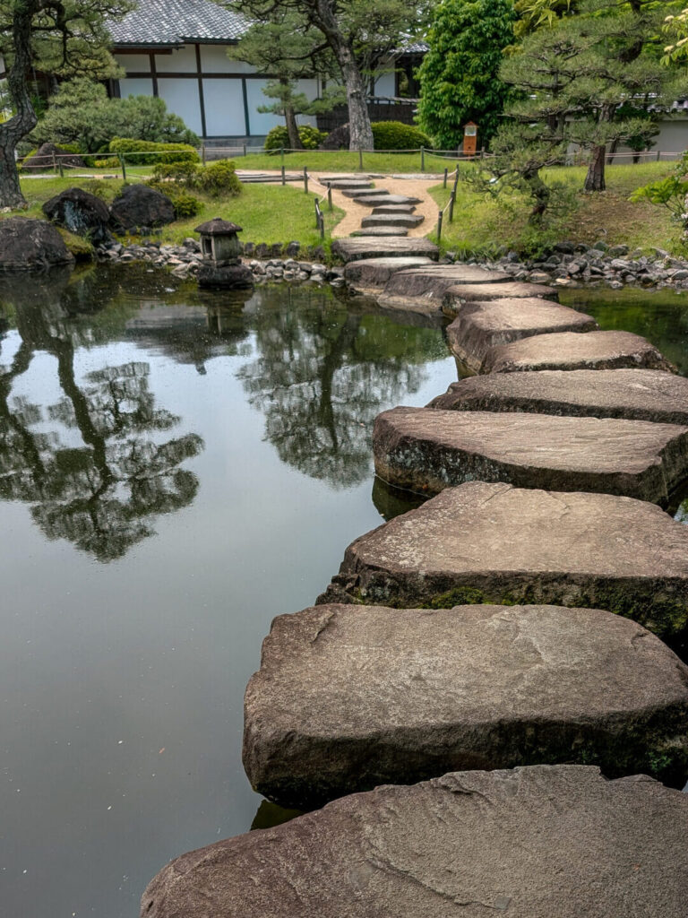A stone path on a lake leading to a Japanese garden and building