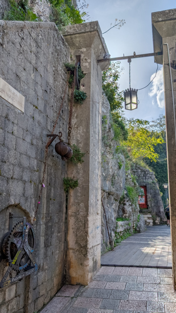 The historic stone North River Gate entrance in Kotor featuring ancient counterweight pulleys, an iron lantern, and a stone walkway.