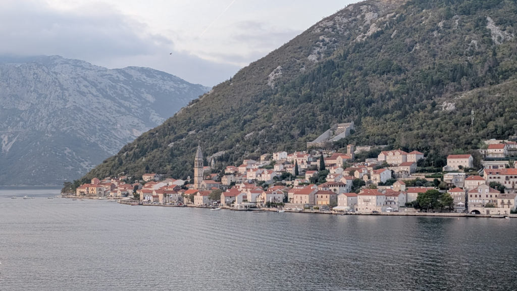 A wide view from the water showing the picturesque coastal town of Perast with its historic church bell tower along the Bay of Kotor.
