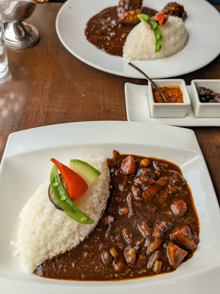 Two plates of Japanese curry with rice and colorful vegetable garnishes served on a wooden dining table in Nara.