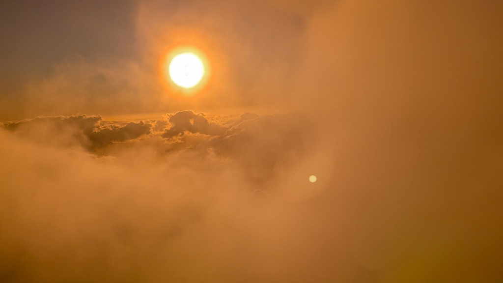 The bright sun shining through thick orange and golden mist during golden hour at Haleakala summit, casting a warm glow over a sea of clouds.